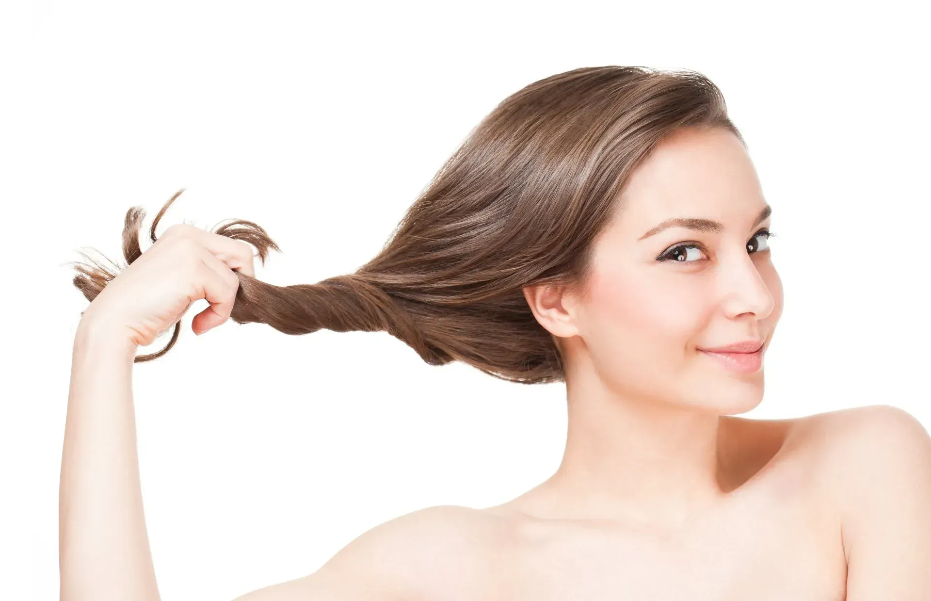 Woman with long brown hair smiles and holds a section of her hair in her hand against a white background.