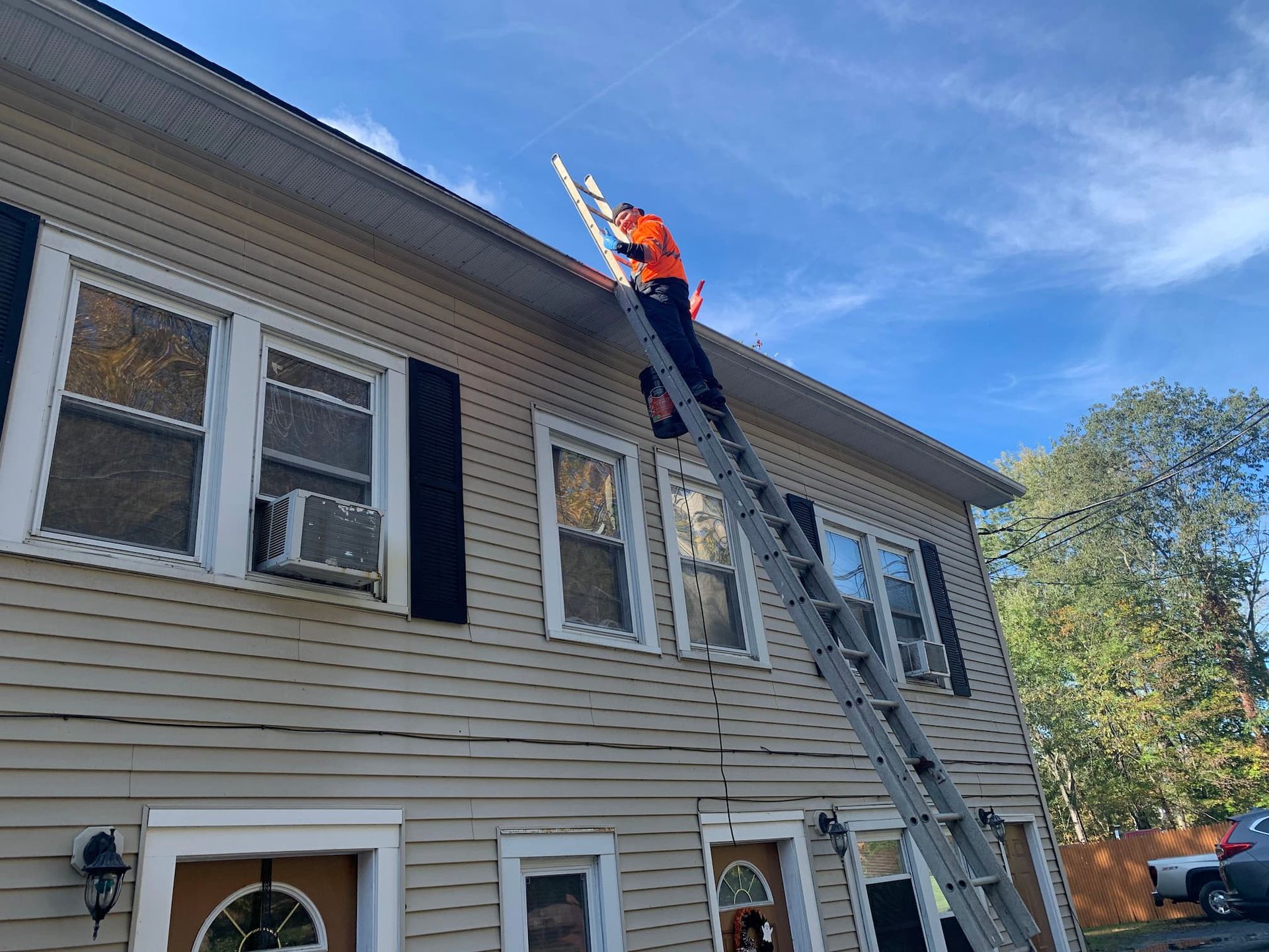 Man On Ladder Cleaning Roof Gutters