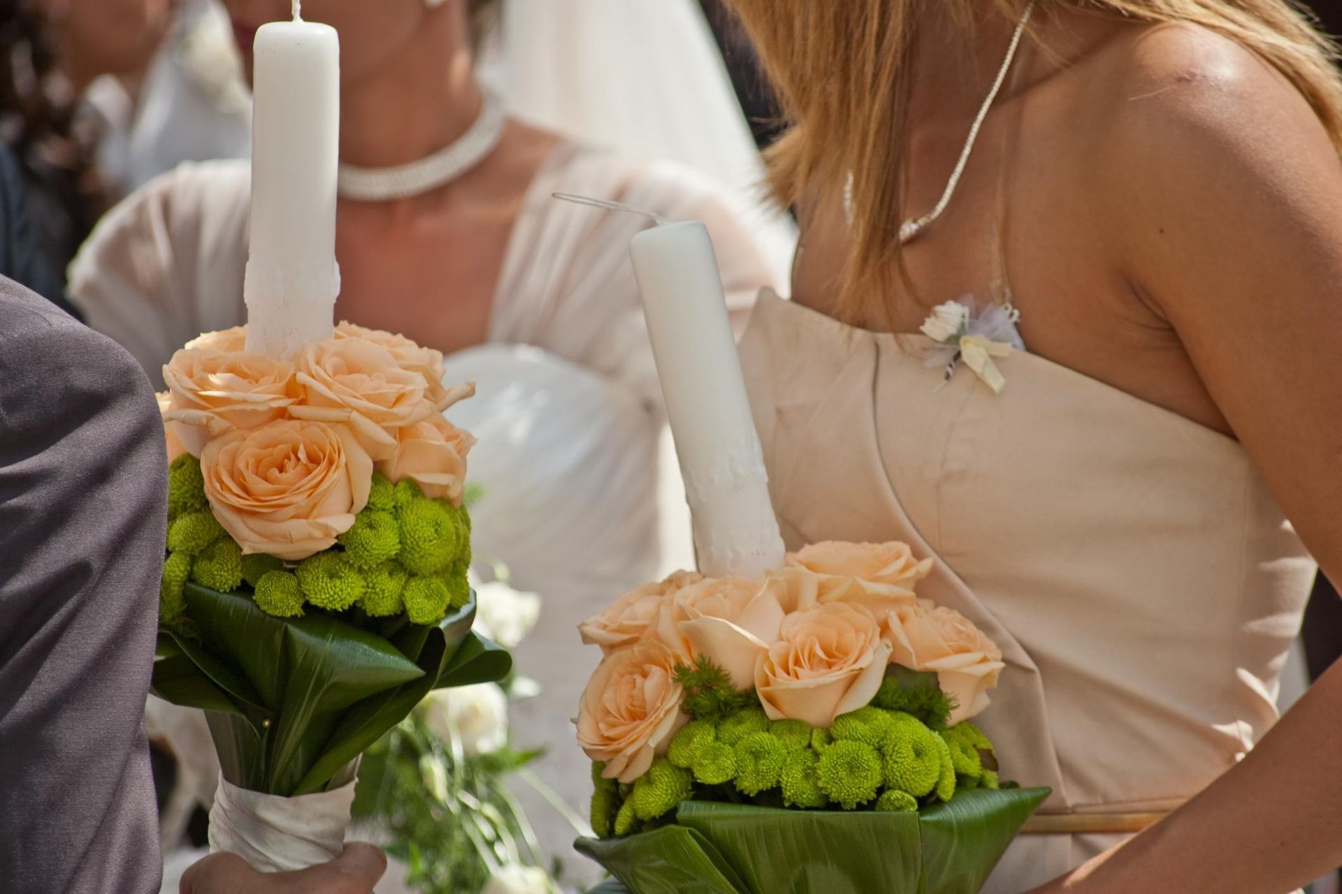 Bouquets of peach roses and green hydrangeas beside white candles at a wedding ceremony