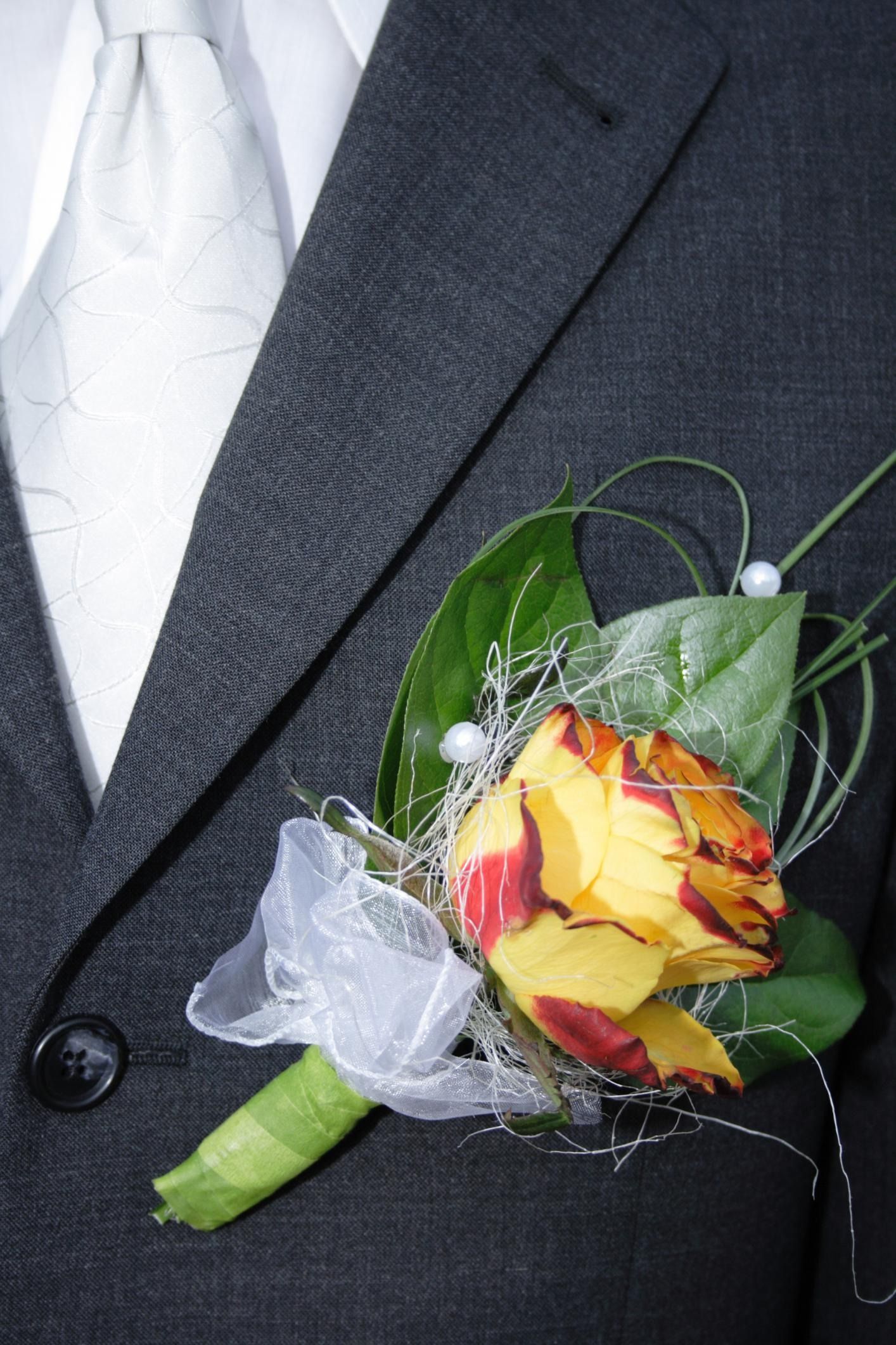 White, yellow, and red boutonniere pinned to a dark suit jacket with a white tie visible