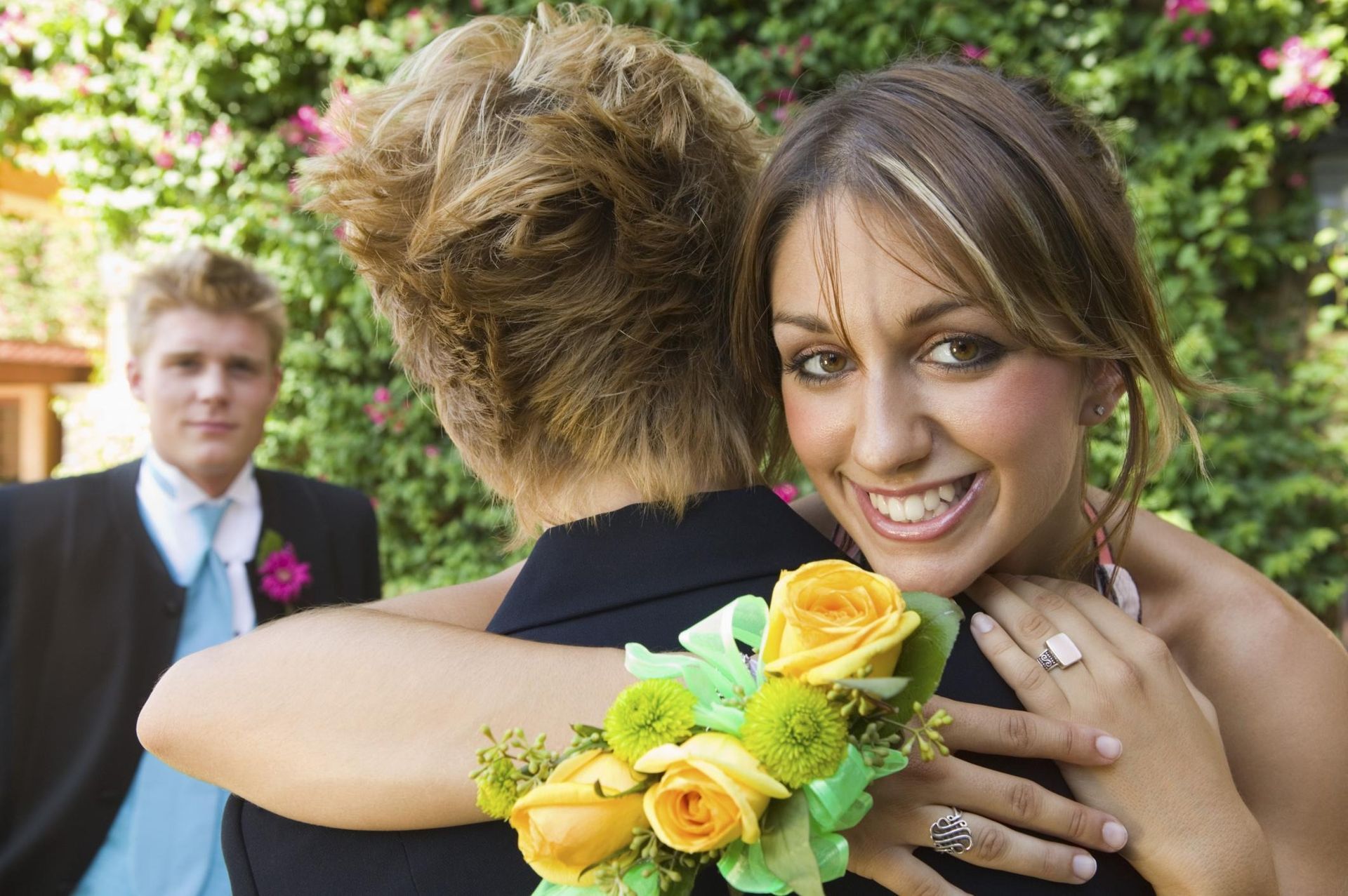 Bride hugging a guest while smiling at a wedding, with yellow roses in the foreground