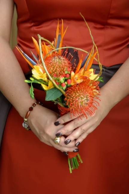Person in a red dress holding a small bouquet of orange and yellow flowers