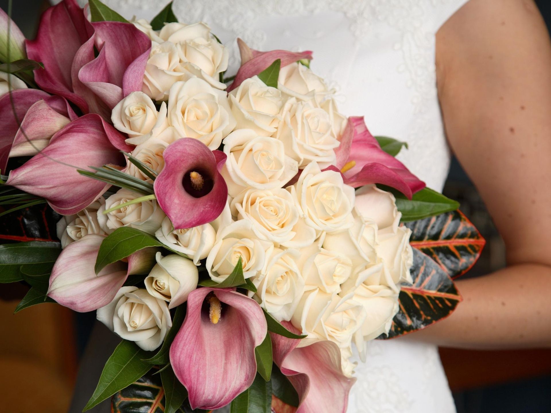 Bouquet of pink lilies, cream roses, and greenery held against a white dress