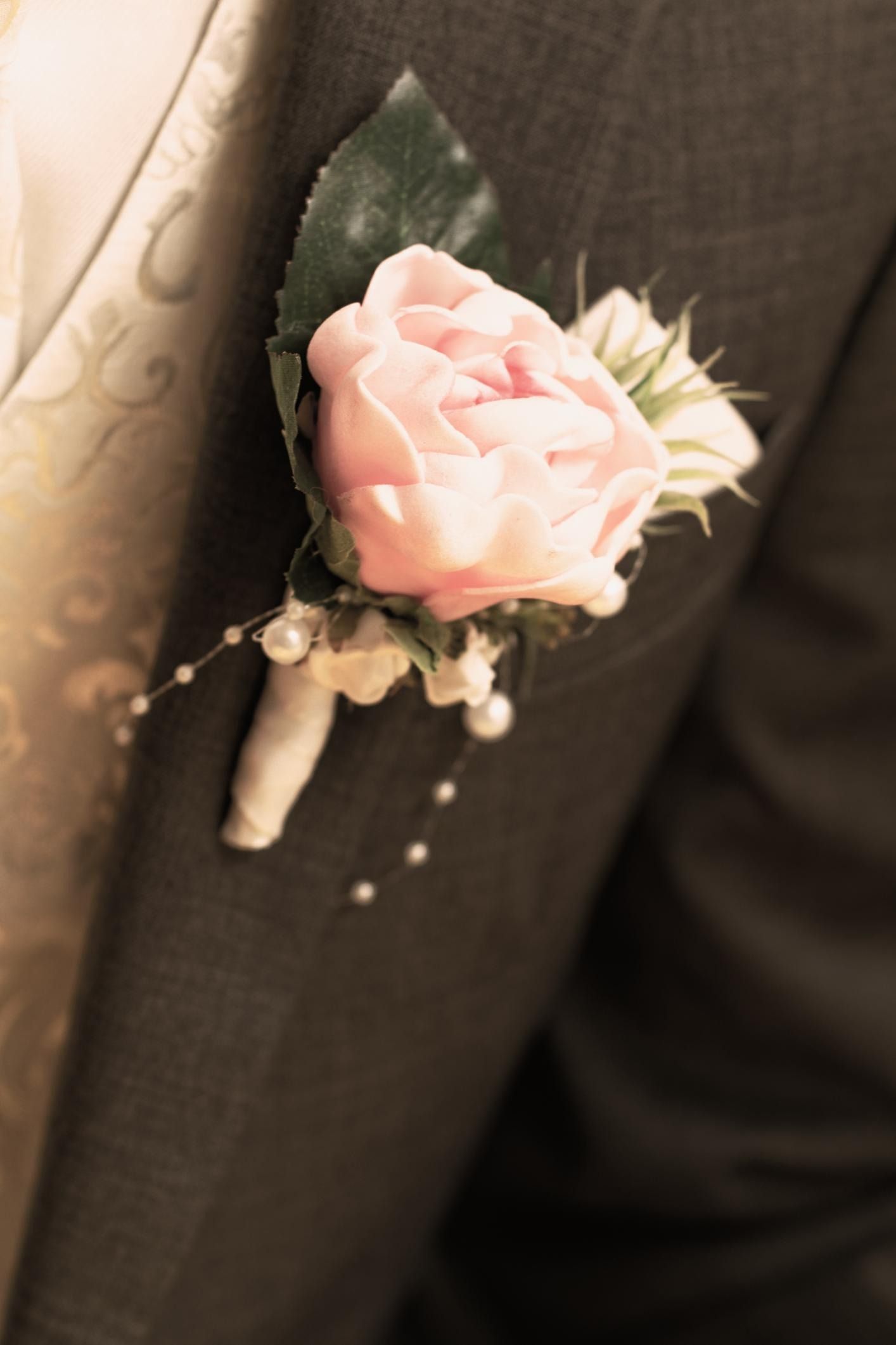 Pink boutonniere pinned to a dark suit lapel, with pearl accents and green leaves