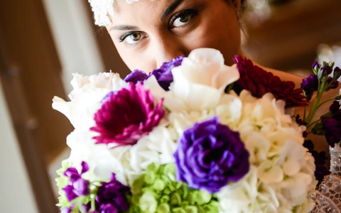 Person peeking over a bouquet of white, purple, and magenta flowers