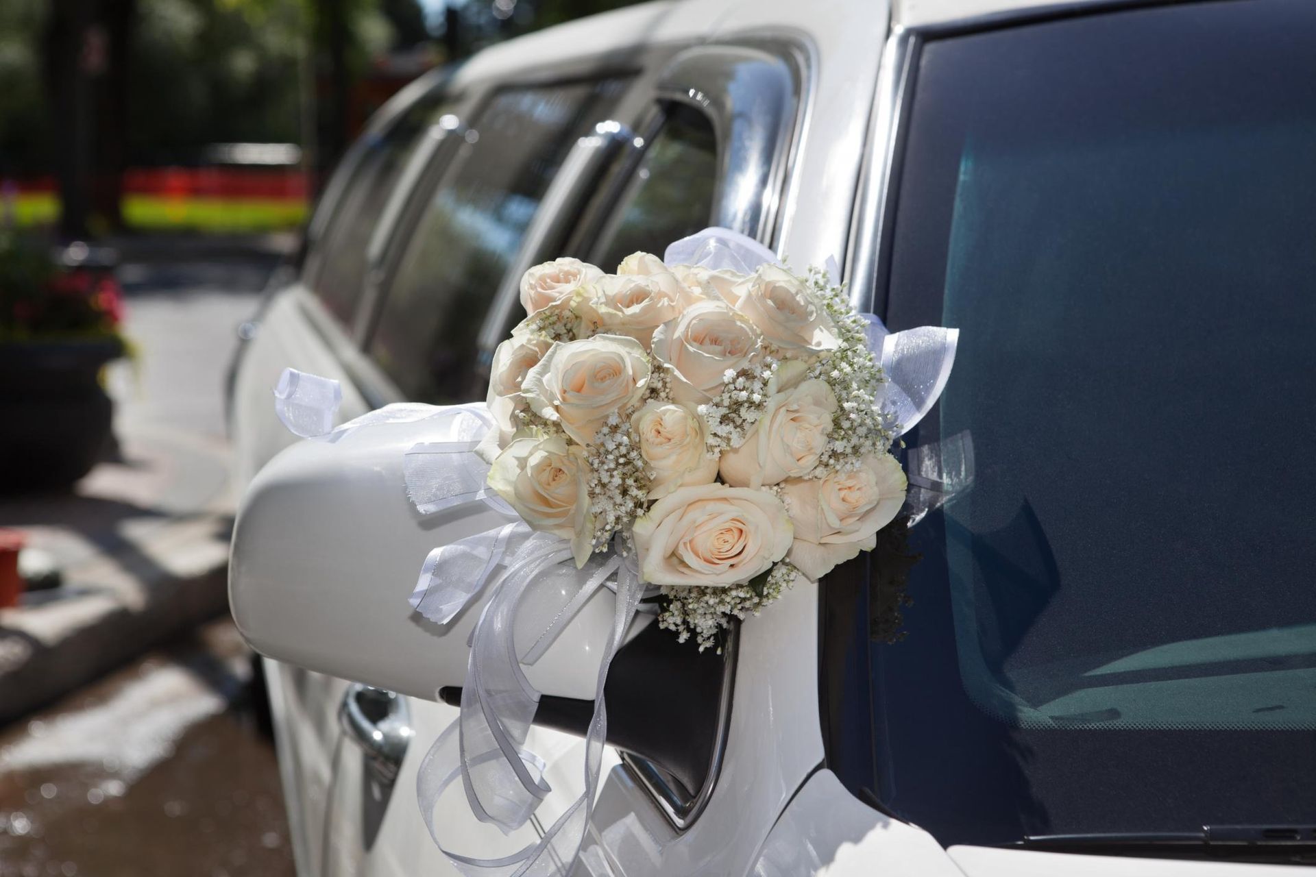 White wedding bouquet tied to a white car mirror on a sunny street