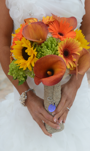 Bridal bouquet with orange, yellow, and green flowers held by a person in a white dress