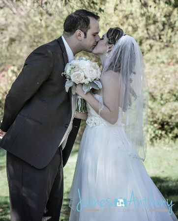 Bride and groom kiss outdoors, bride holding white bouquet in a white gown and veil.