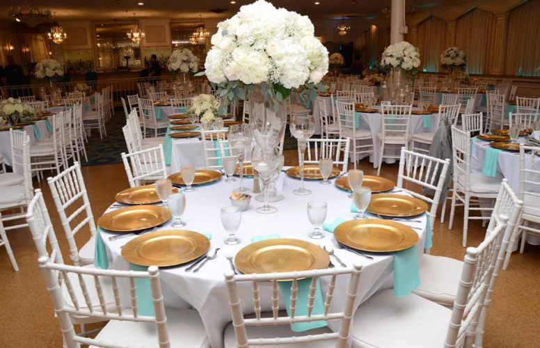Round banquet tables set with gold plates and white chairs in a decorated reception hall
