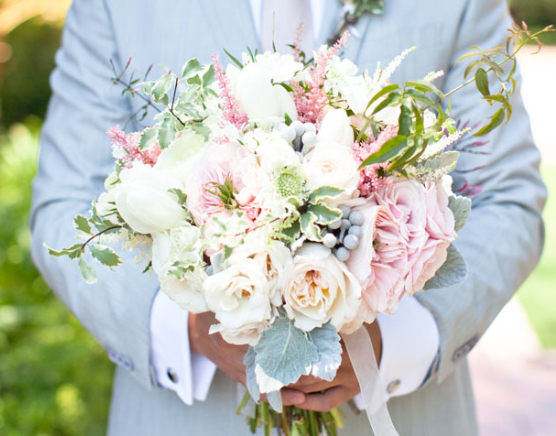 Person holding a white and blush pink bridal bouquet outdoors