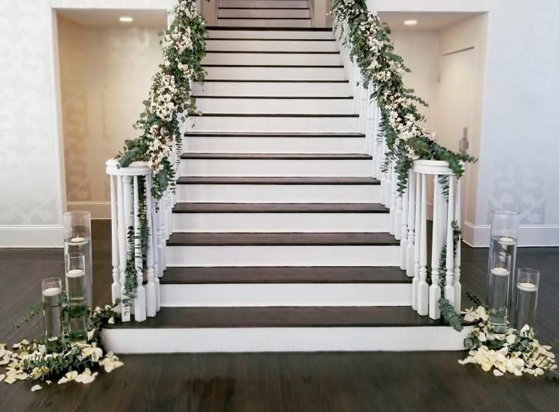 Decorated white staircase with floral garlands and lanterns in an elegant indoor entryway