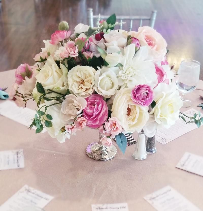 Pink and white rose bouquet centerpiece on a round table with place cards and glassware