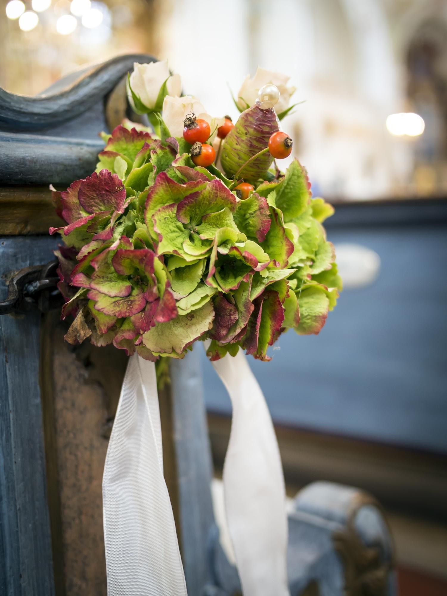 Green and pink bouquet with white ribbons tied to a dark post, softly lit in the background