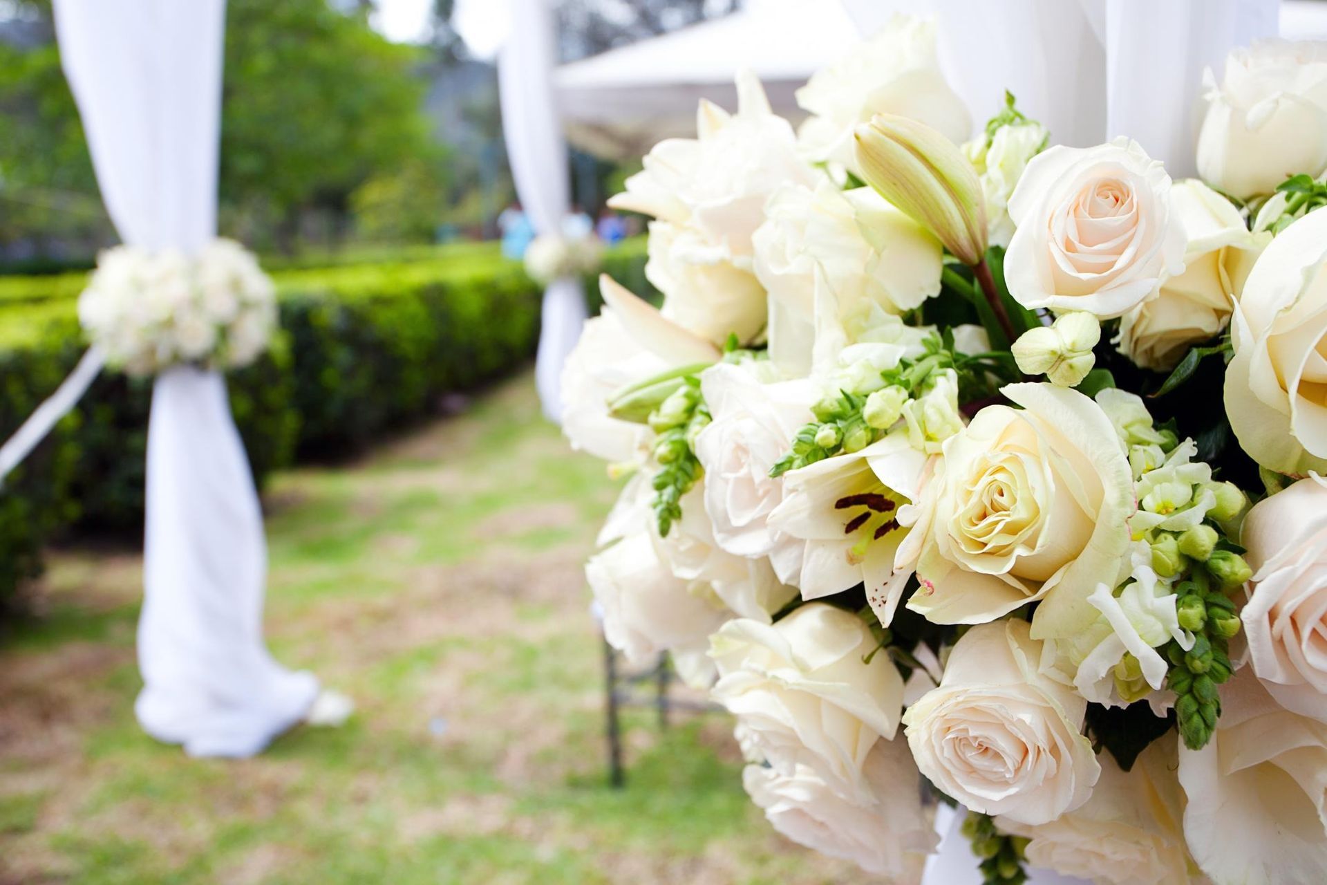 Cream roses and white flowers in a wedding bouquet at an outdoor ceremony aisle.