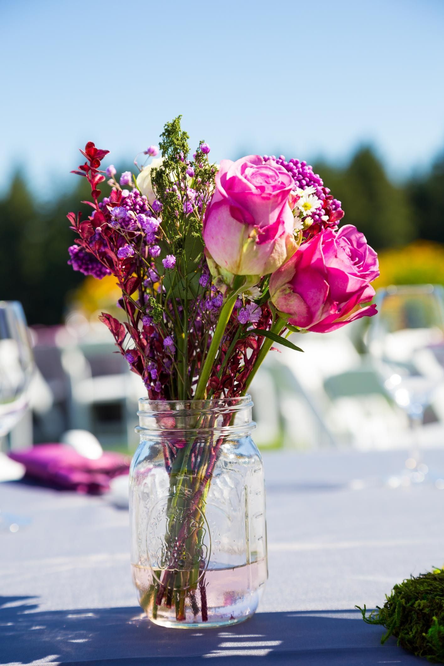 Pink and purple flowers in a glass vase on an outdoor table with chairs blurred in the background