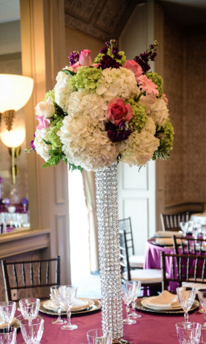Tall crystal vase with white, pink, and purple floral arrangement on a set dining table in a formal room