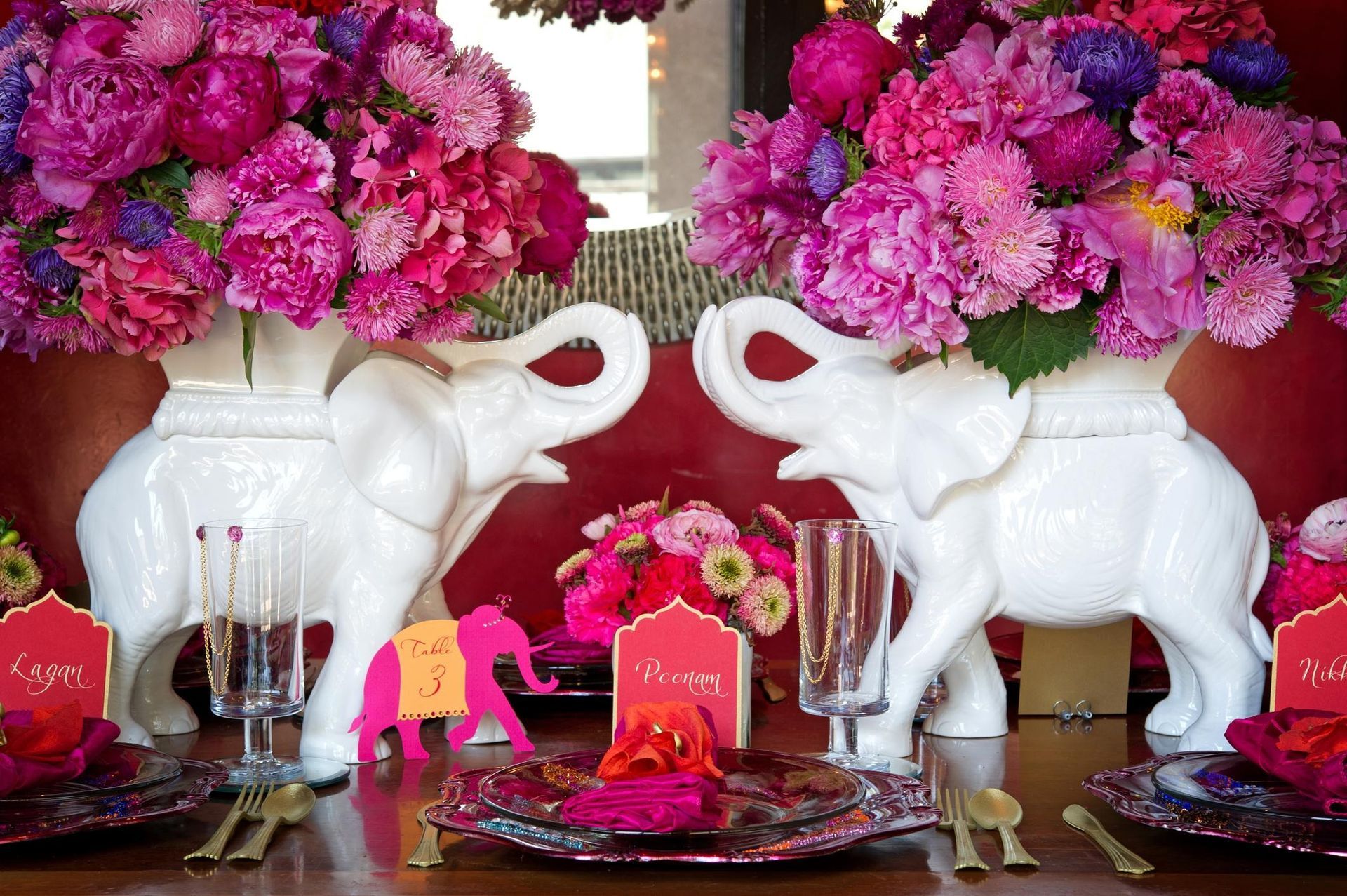 Pink and purple floral centerpiece with white elephant figurines and place settings on a decorated table.