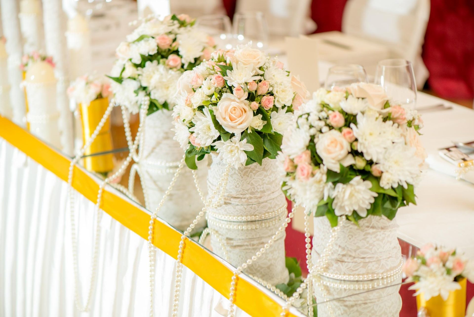 White floral arrangements in rope-wrapped vases on a decorated table with yellow and white ribbon accents