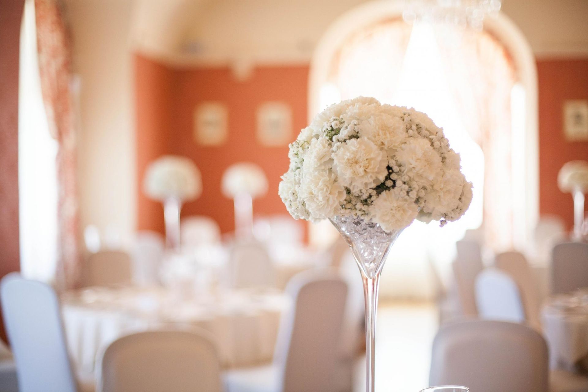White floral centerpiece in a decorated wedding reception hall with soft orange walls and round tables