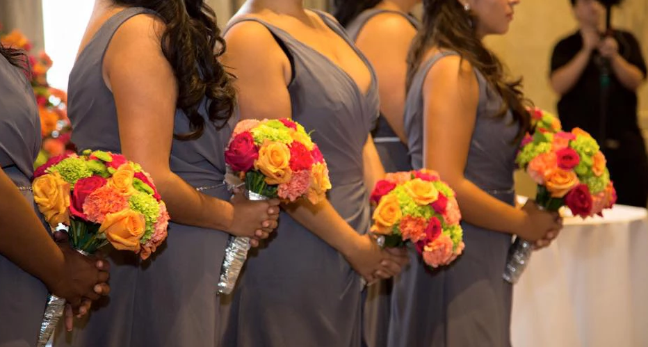 Bridesmaids in gray dresses holding bright floral bouquets during a ceremony