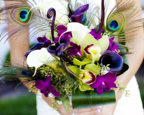 White, purple, and green floral bouquet with peacock feathers and orchids in a glass vase
