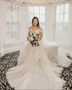 Bride in a white gown holding a bouquet in a bright room with patterned black-and-white carpet
