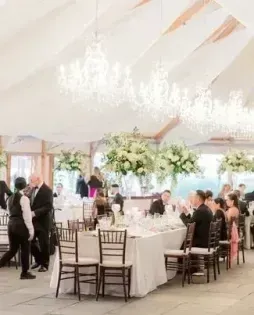 Elegant indoor wedding reception with white floral centerpieces and guests seated at long tables