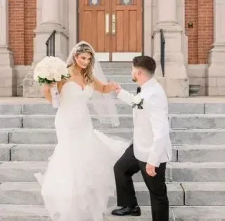 Bride and groom on church steps, holding hands with bouquet and white wedding attire