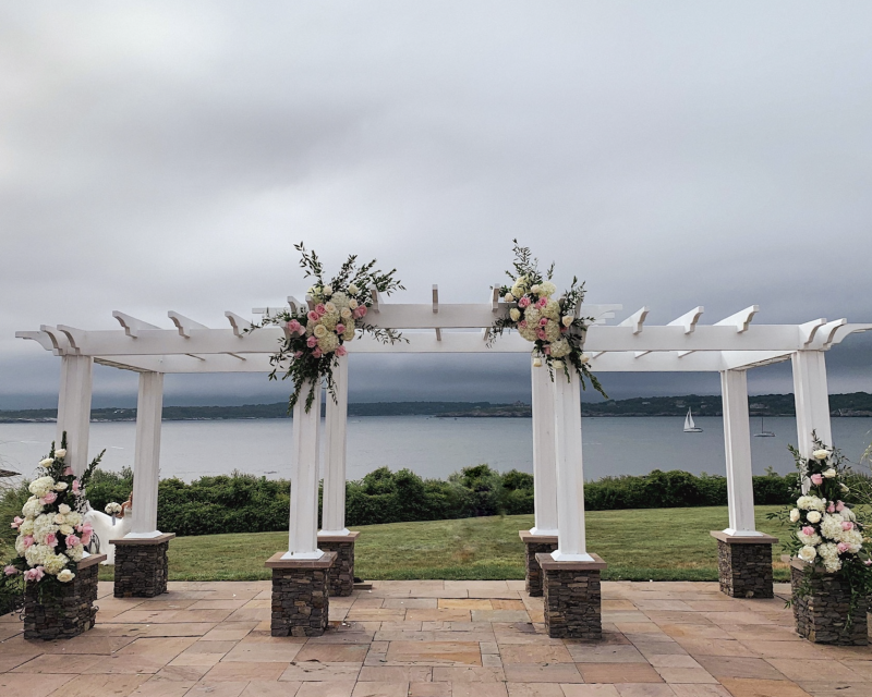Floral-decorated outdoor wedding arch overlooking a lake under a cloudy sky