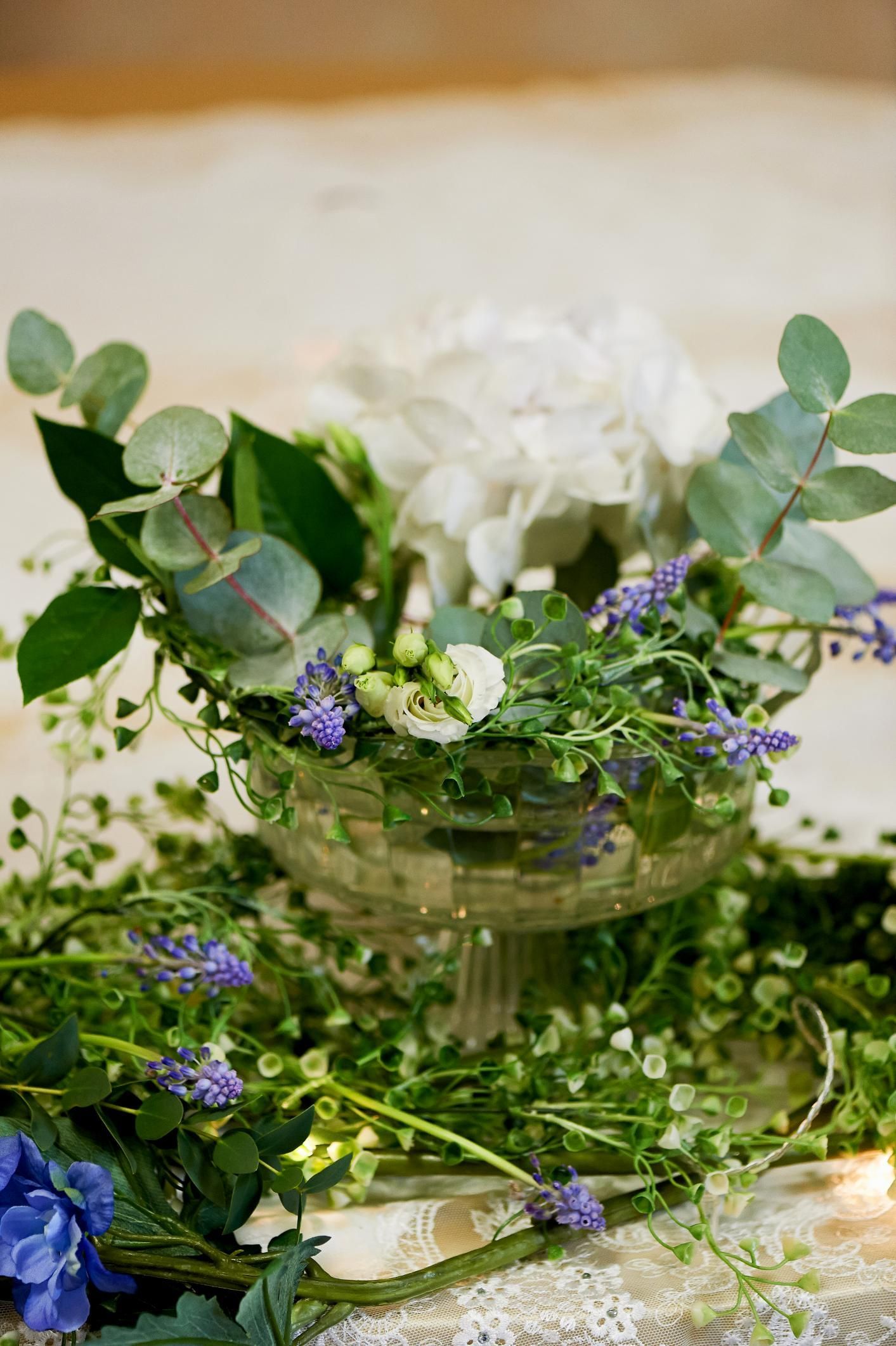 White and purple flowers with greenery arranged in a glass vase on a table