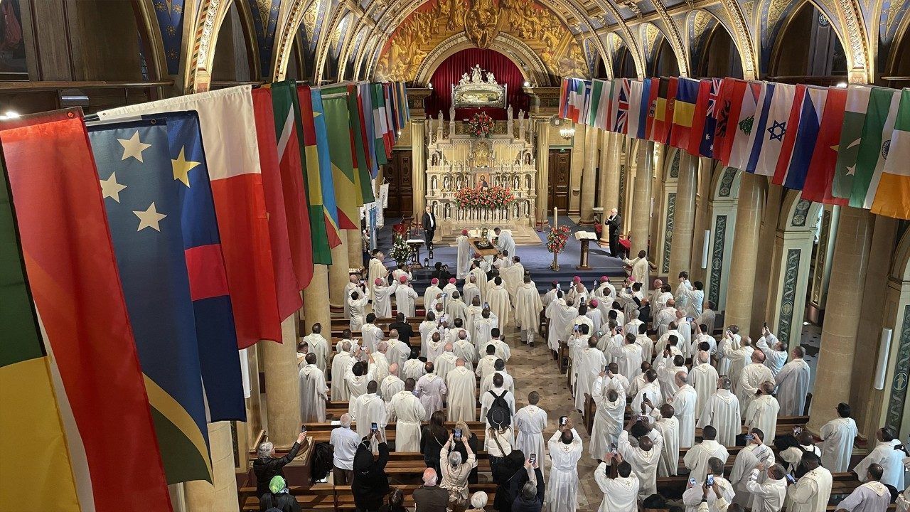 Large church gathering with white-robed people, flags hanging. Altar in the background.