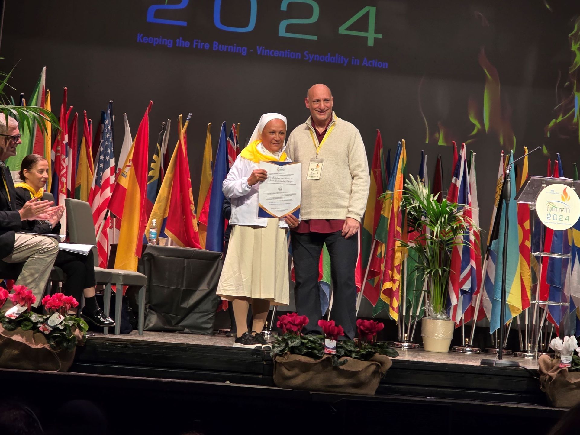 A man and a woman are standing on a stage in front of a sign that says 2024