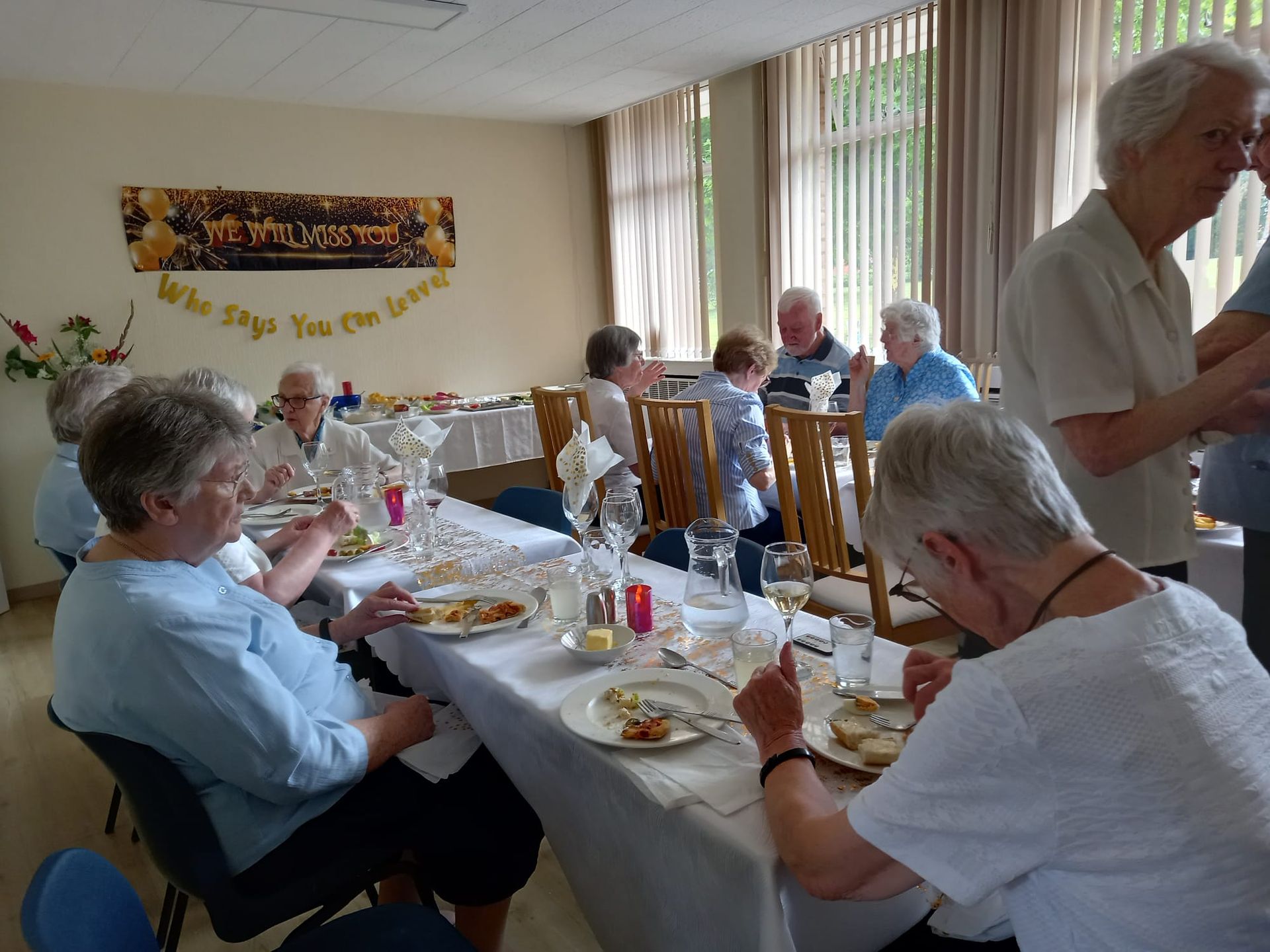 Senior citizens at a luncheon, eating at a table, in a brightly lit room.