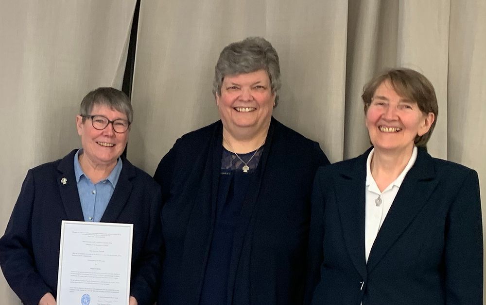 Three women are standing next to each other and smiling while holding a certificate.