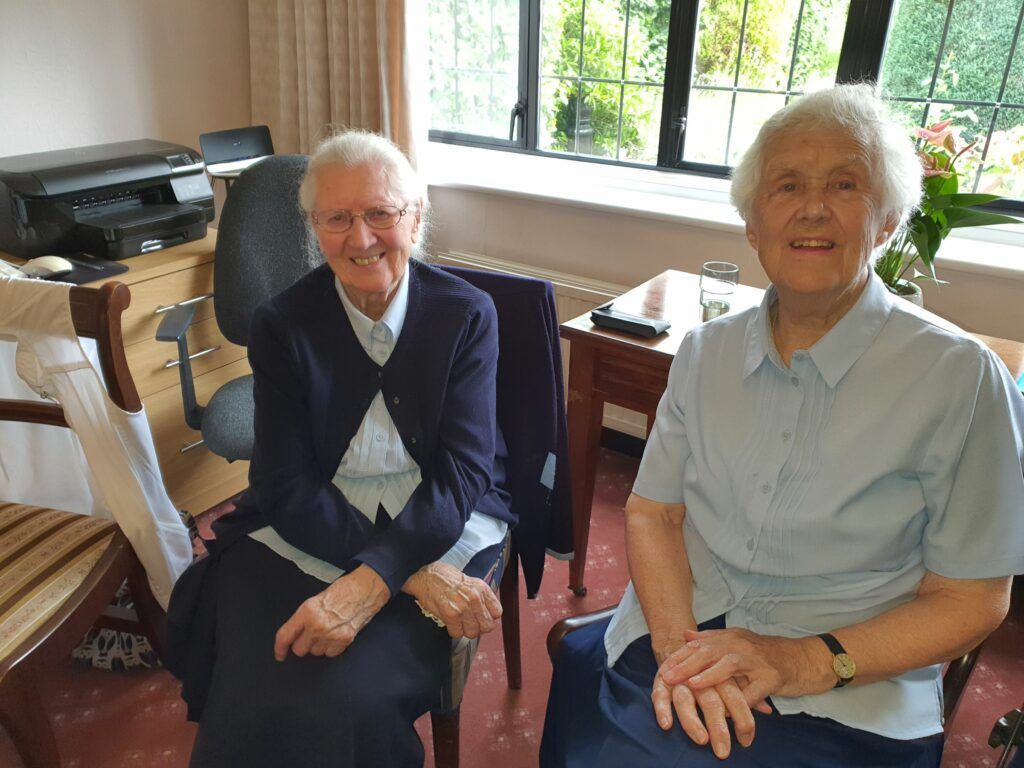 Two elderly women are sitting next to each other in a room.