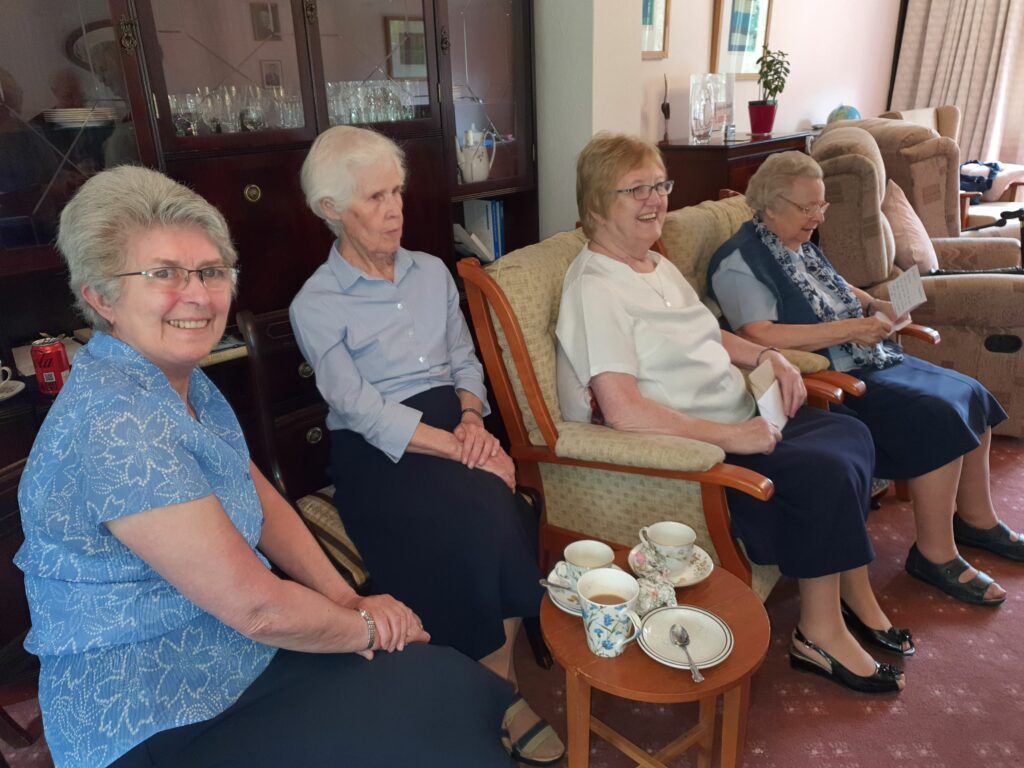 A group of older women are sitting in chairs in a living room