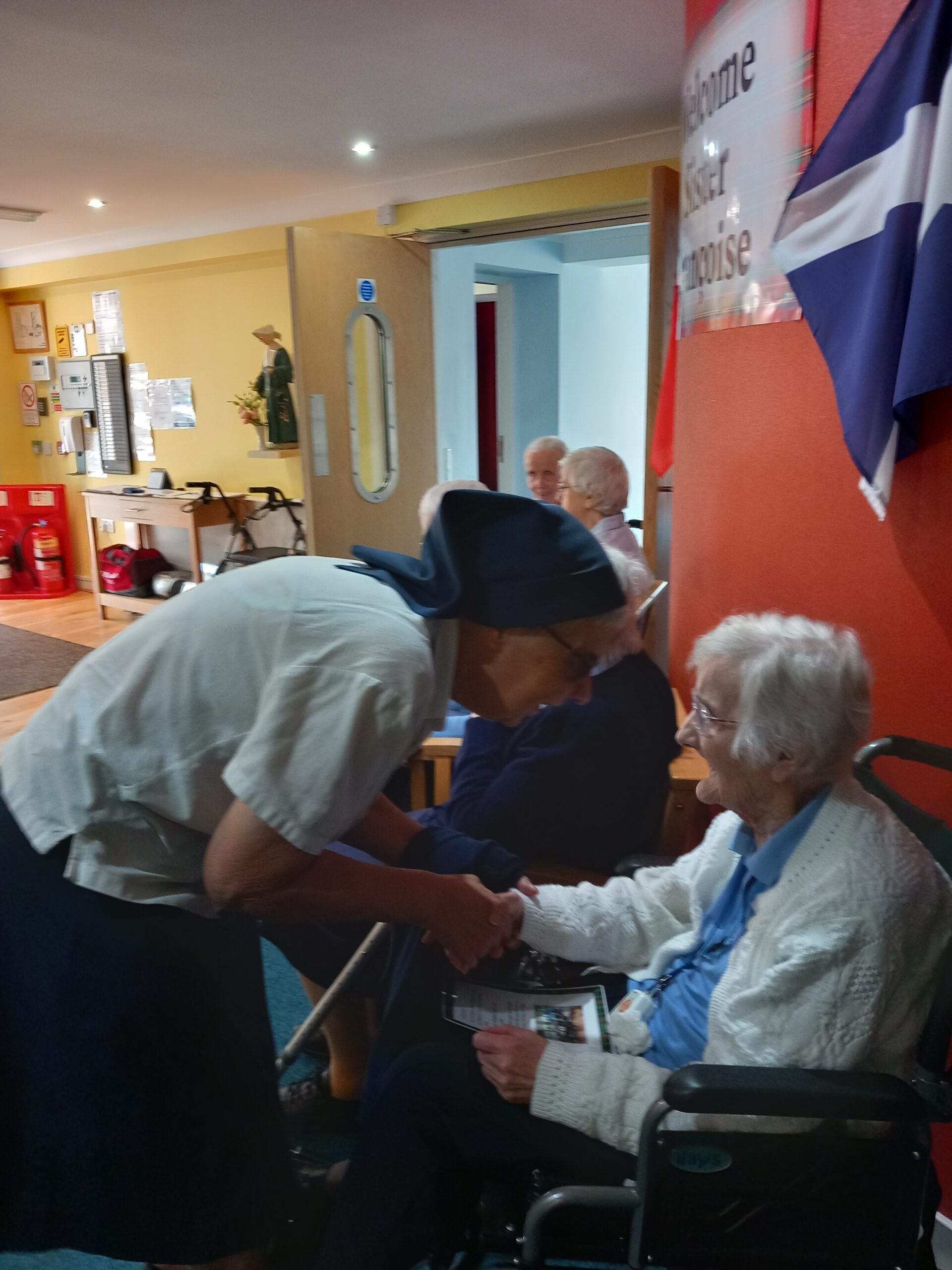 A man in a pirate hat shakes hands with an elderly woman in a wheelchair