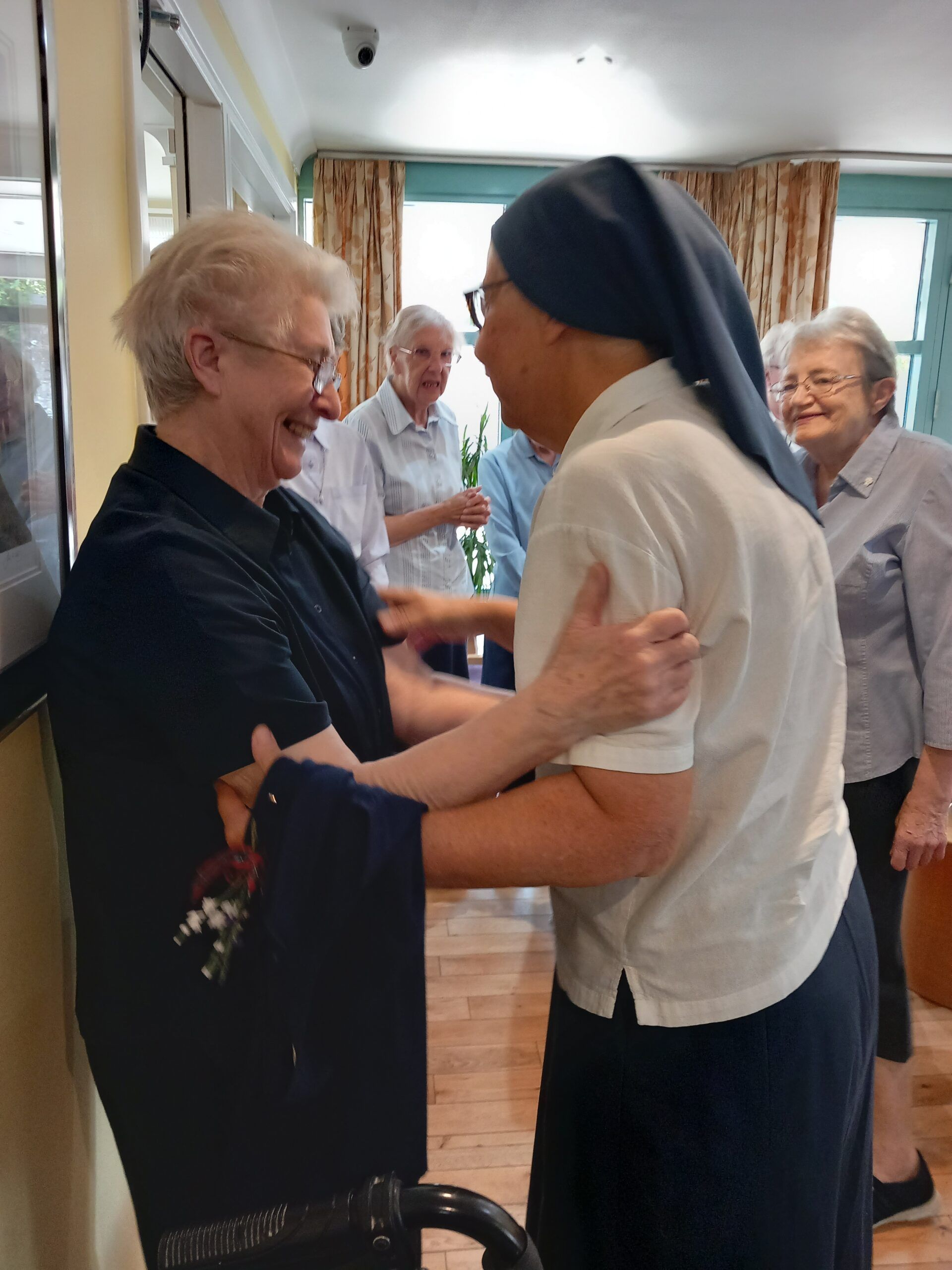 A woman in a nun 's habit is hugging another woman in a room.