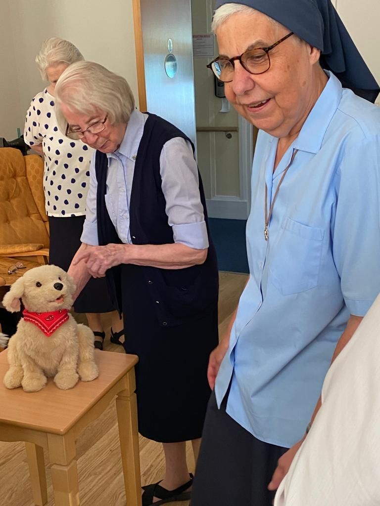 Two elderly women are playing with a stuffed dog on a table.