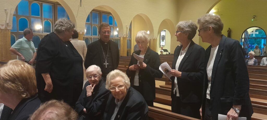 A group of people are standing in a church talking to each other.
