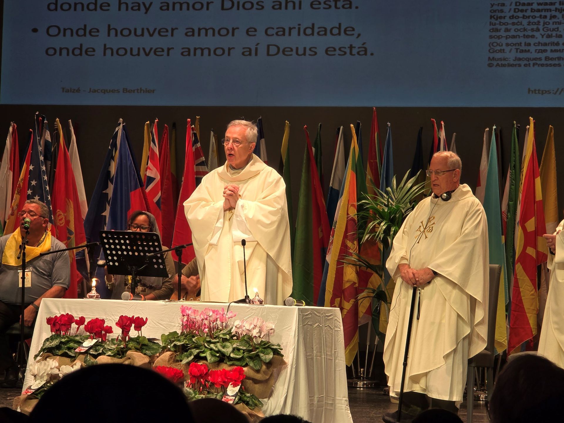 Two priests are standing in front of a table with flowers and a sign that says donde hay amor dios ani esta