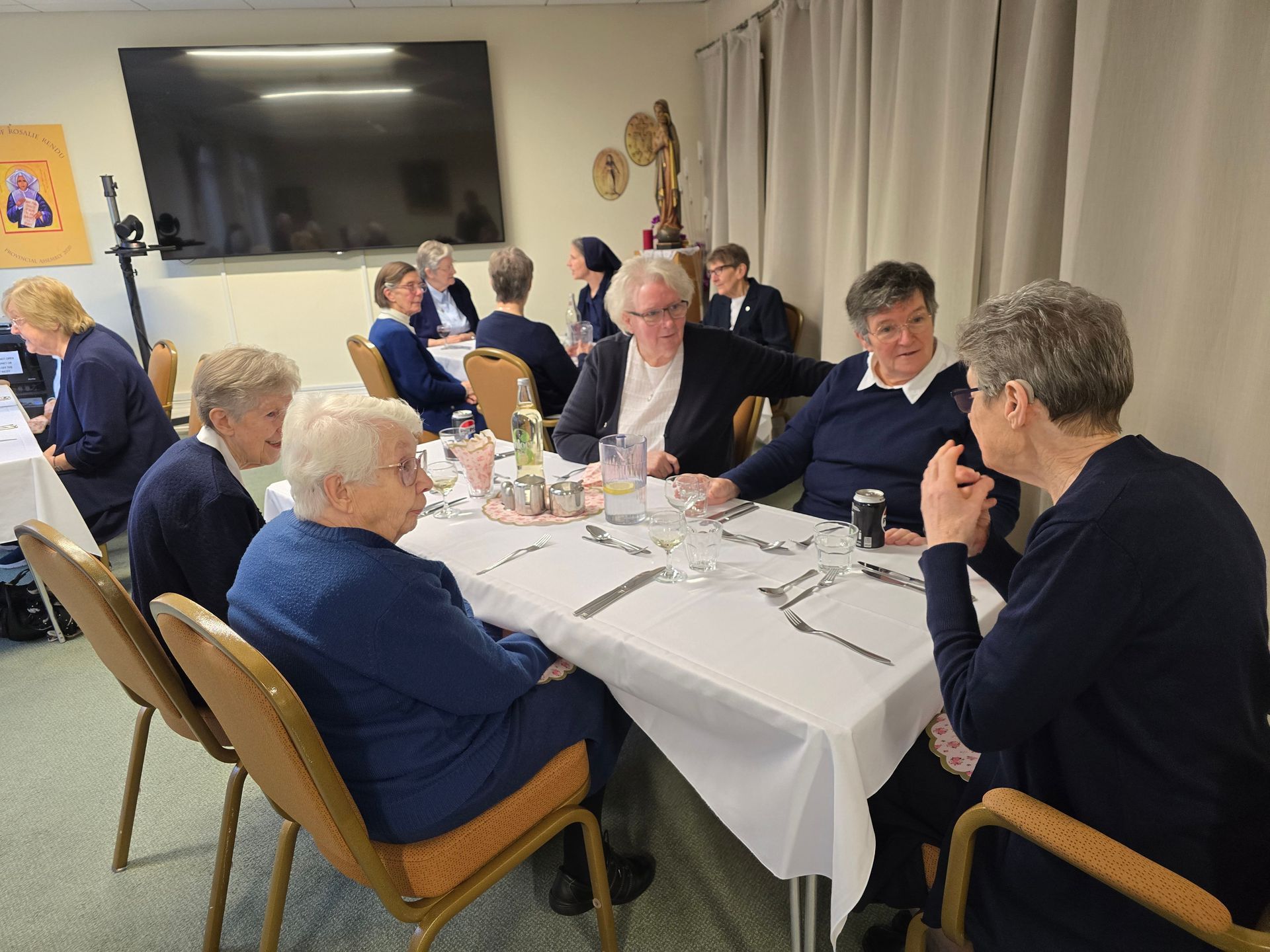 Group of women in blue discussing at a table set for a meal.
