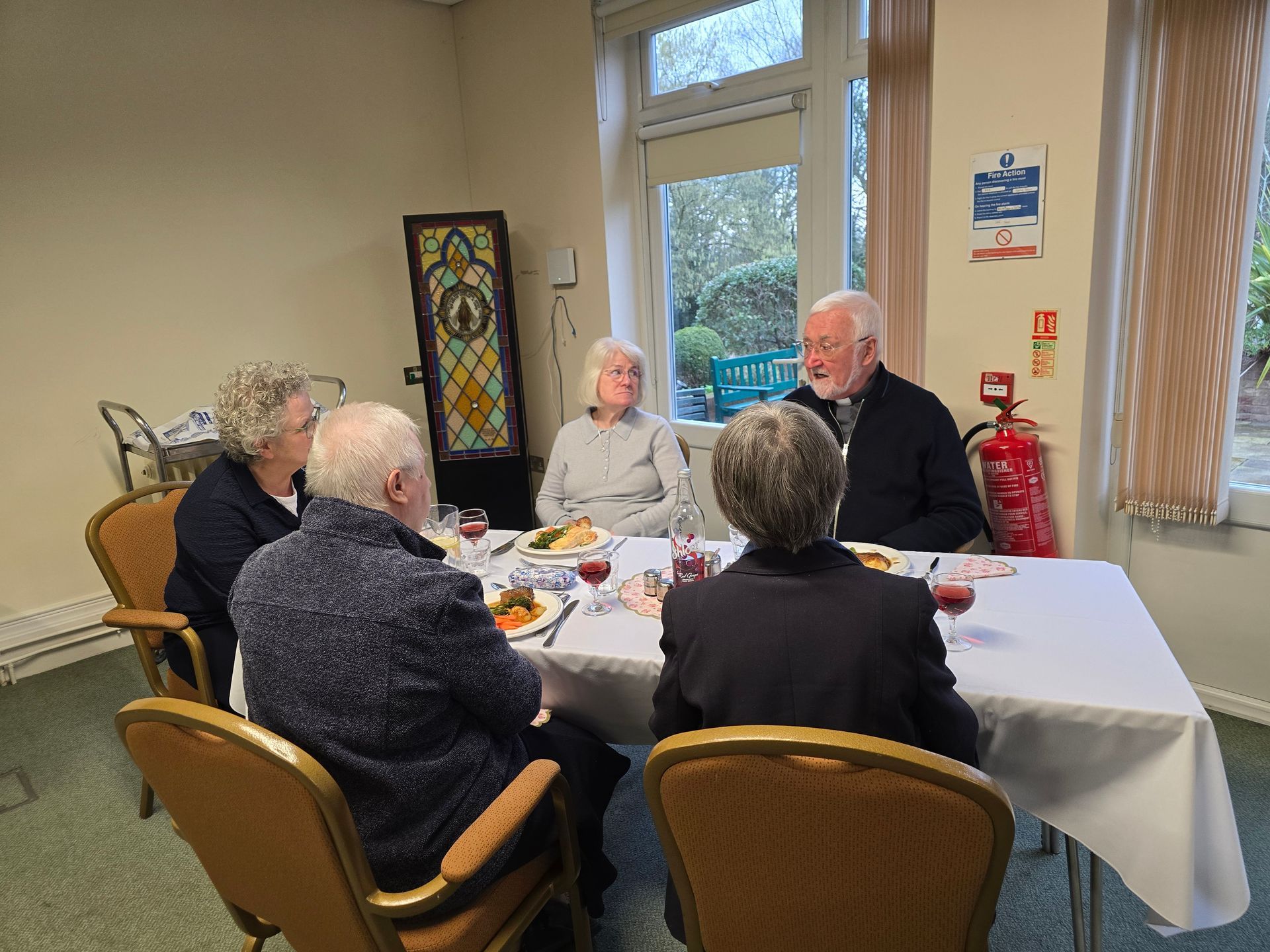 Five seniors seated at a table, dining and conversing in a well-lit room.