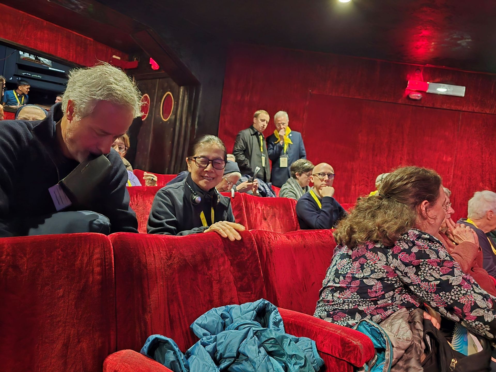 A group of people are sitting in red chairs in a theater.
