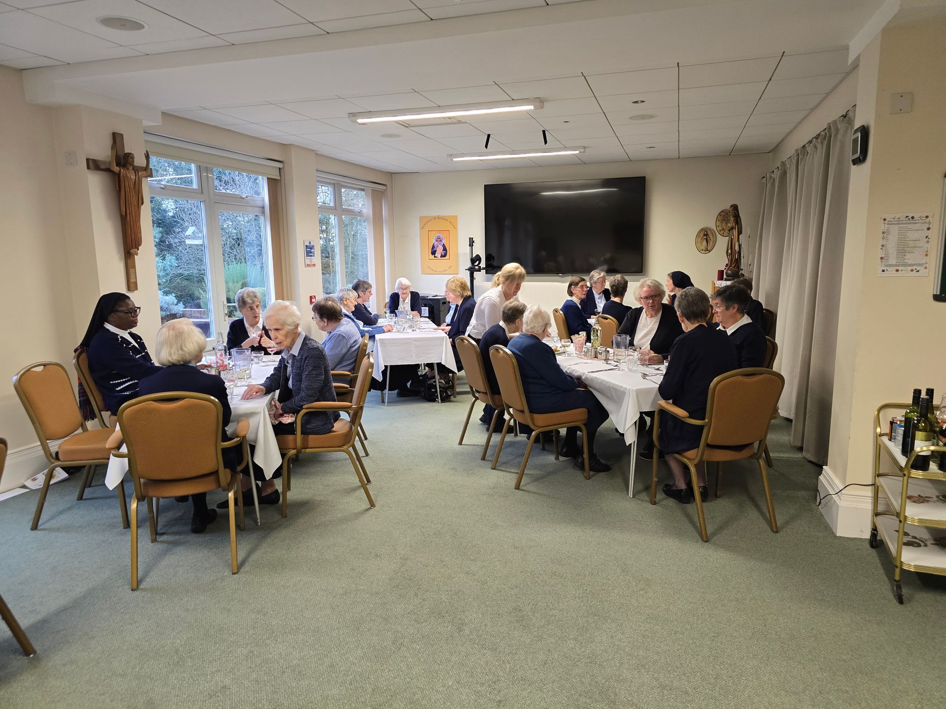 People seated at tables in a well-lit room; a religious gathering, likely a dinner.