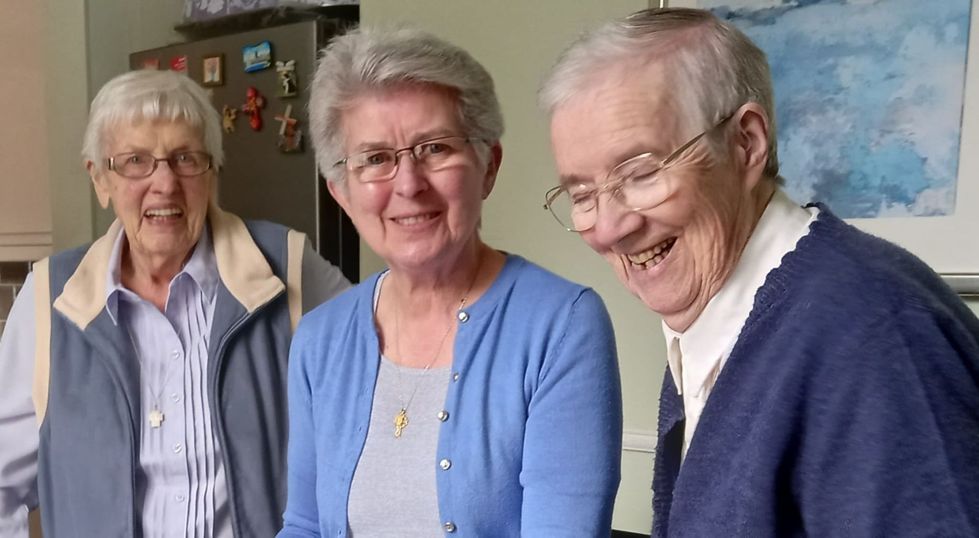 Three elderly women smiling, indoors. One woman is laughing. Blue and white clothing.