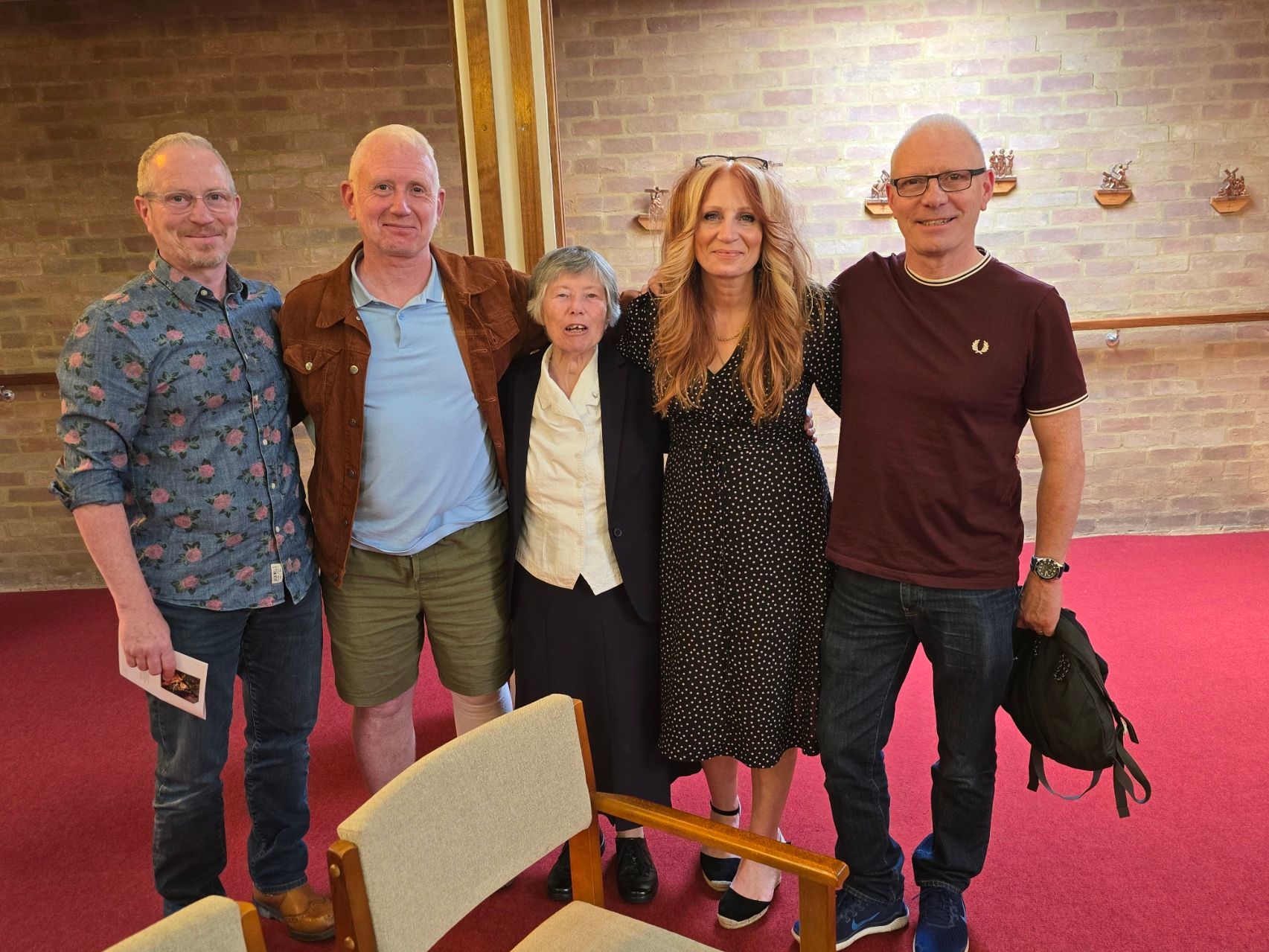 Five people stand close together, smiling, in a room with red carpet.