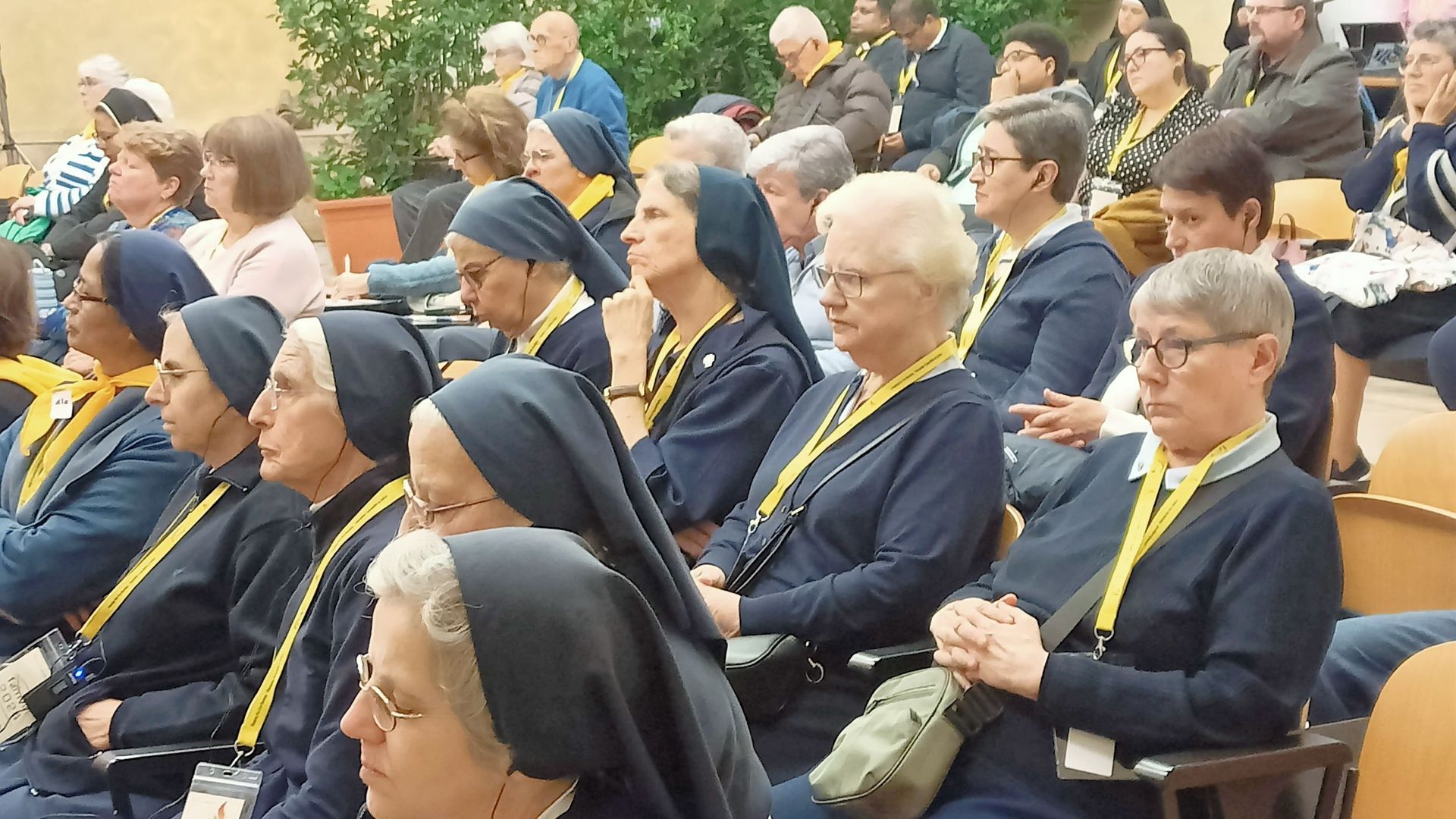 A group of nuns are sitting in a row with other people