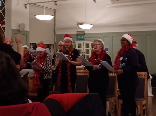 A group of people wearing santa hats are singing in a room