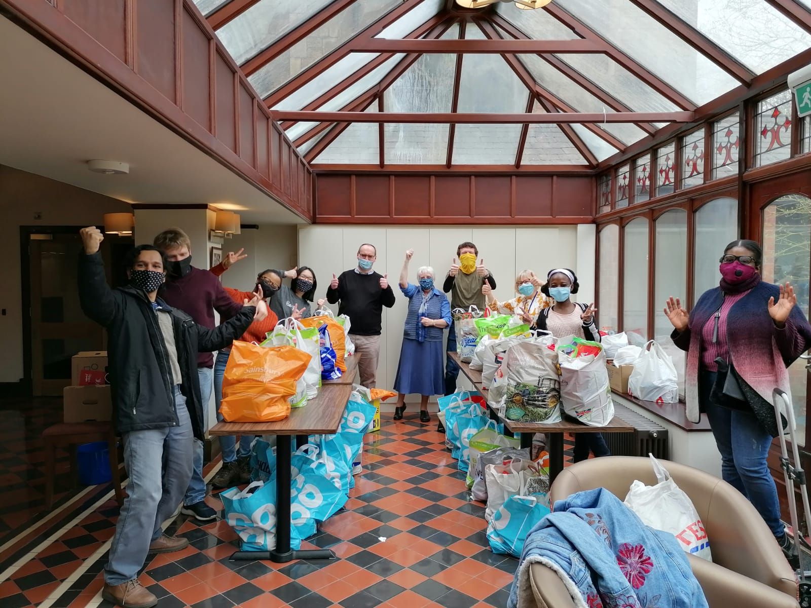 A group of people wearing masks are standing in a room filled with bags.
